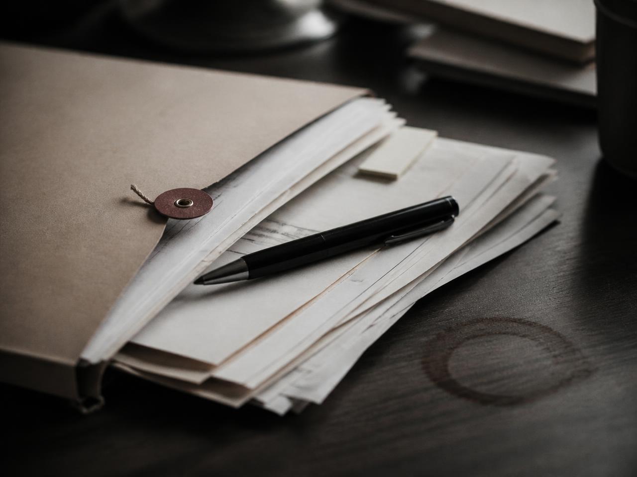 A manila case file with papers fanned out and a pen resting on top
